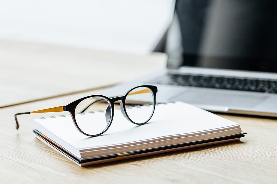 Business Insurance Glossary - Desk With Glasses, Notebook and Computer Laid Out