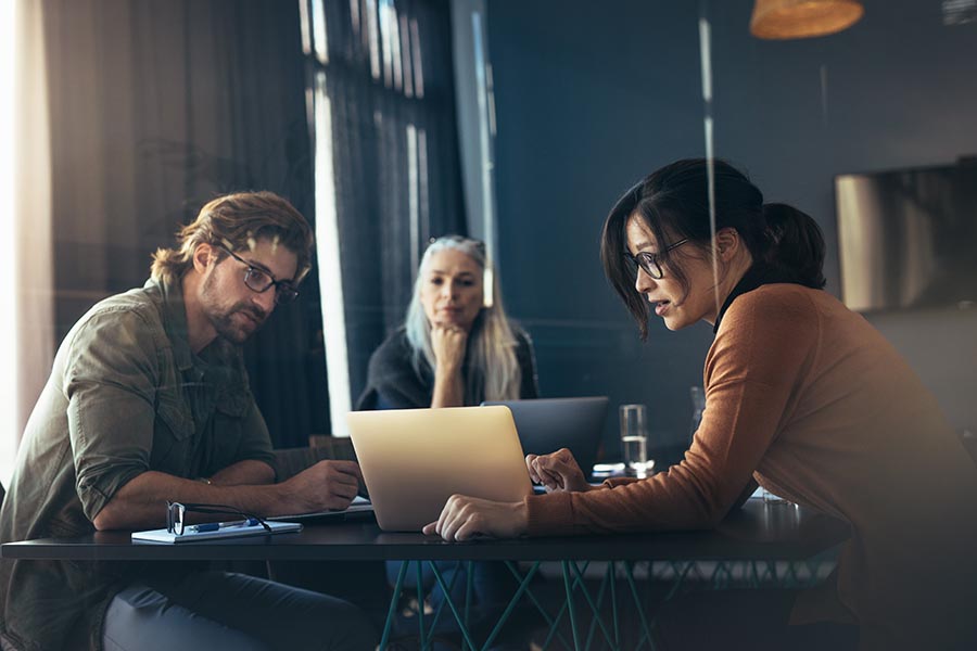 Understanding Your Insurance Audit - Three Coworkers Reviewing a Laptop in a Cozy, Dimly Lit Office